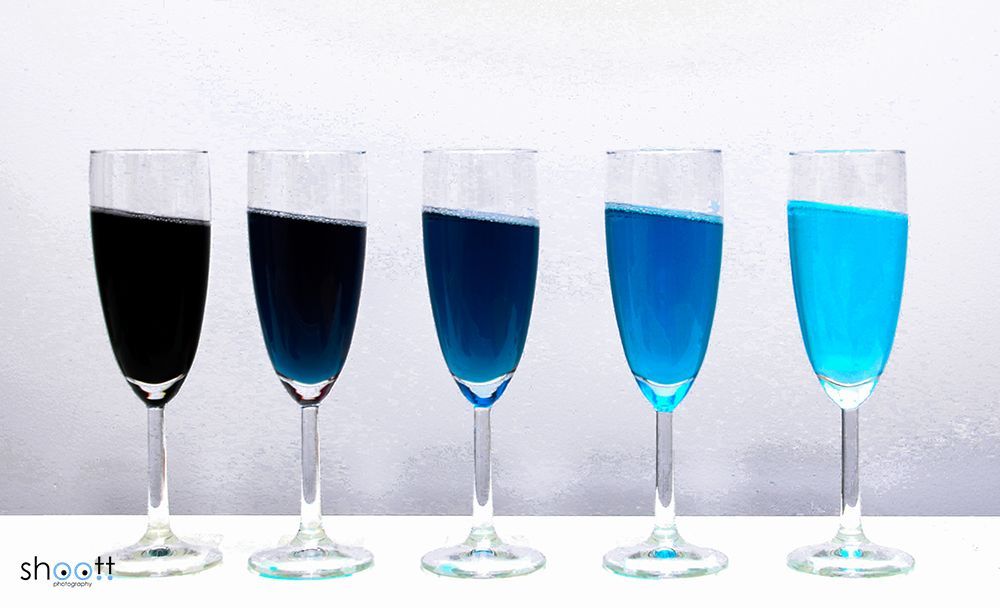 Vijf champagneglazen staan ​​op een rij op een witte ondergrond, met een kleurovergang van diep donkerblauw naar lichtblauw.