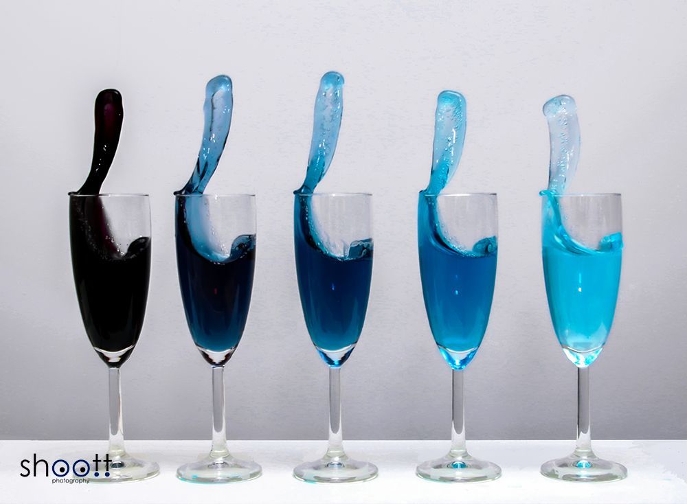 Vijf champagneglazen op een rij, elk gevuld met een vloeistof met een blauwe kleurovergang van donkerblauw tot helder cyaan.