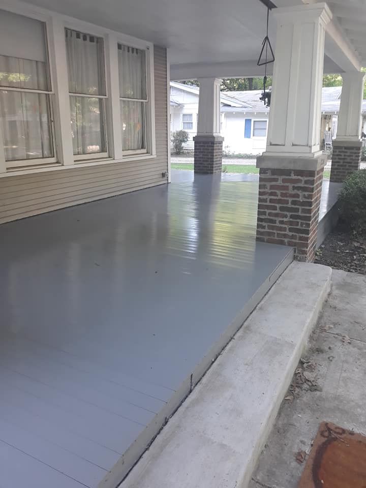 A porch with a gray concrete floor and brick pillars on a house.