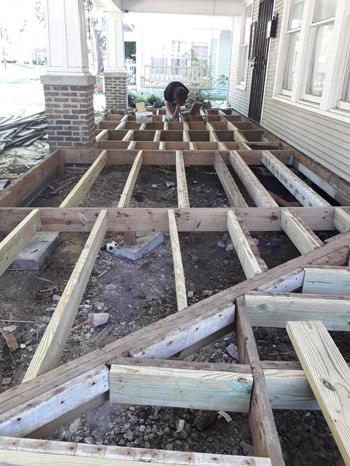 A man is working on a wooden deck under a porch.