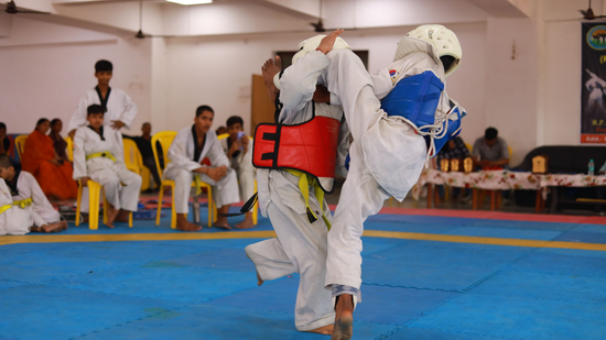 Two martial artists sparring in protective gear on a blue mat during a competition