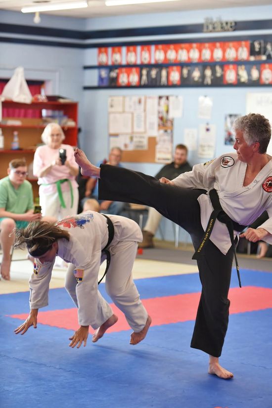 Martial arts class with two people practicing kicks and handstands on blue and red mats in a studio
