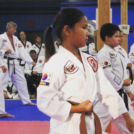 Martial arts students in white gis standing in formation on blue and red mats at a training event