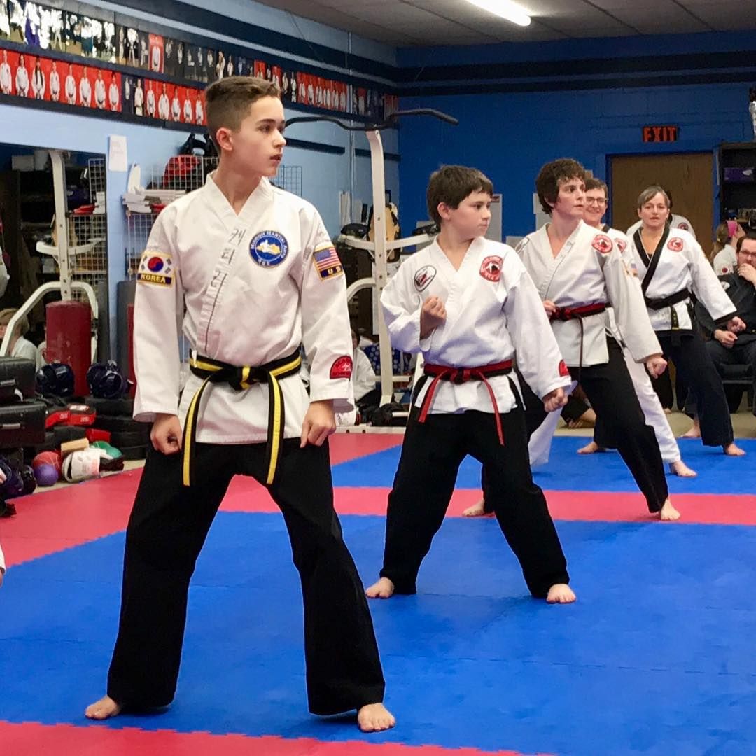 Martial arts students in white uniforms practice stances on blue mats in a dojo.