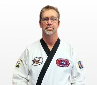 Man in white martial arts uniform with black trim and patches, standing against a plain white background