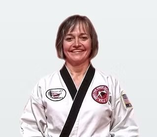 Woman in a white martial arts uniform with black trim, smiling against a plain background.