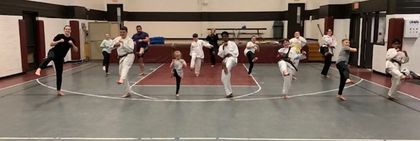 Group of People practicing synchronized moves in a gymnasium, wearing black, white, and red outfits.