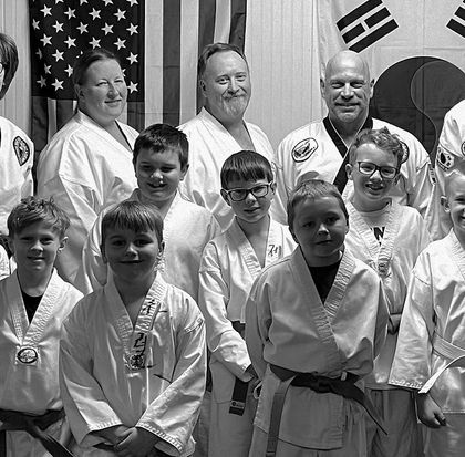 Group of martial arts students and instructors posing in uniforms in front of U.S. and South Korean flags