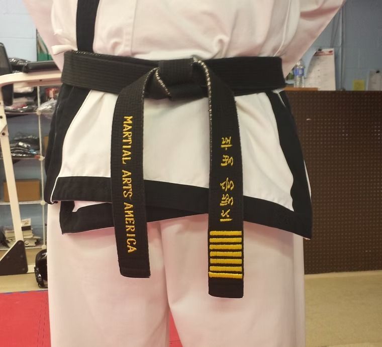Person in a white martial arts uniform with a black belt showing yellow embroidered text and stripes.