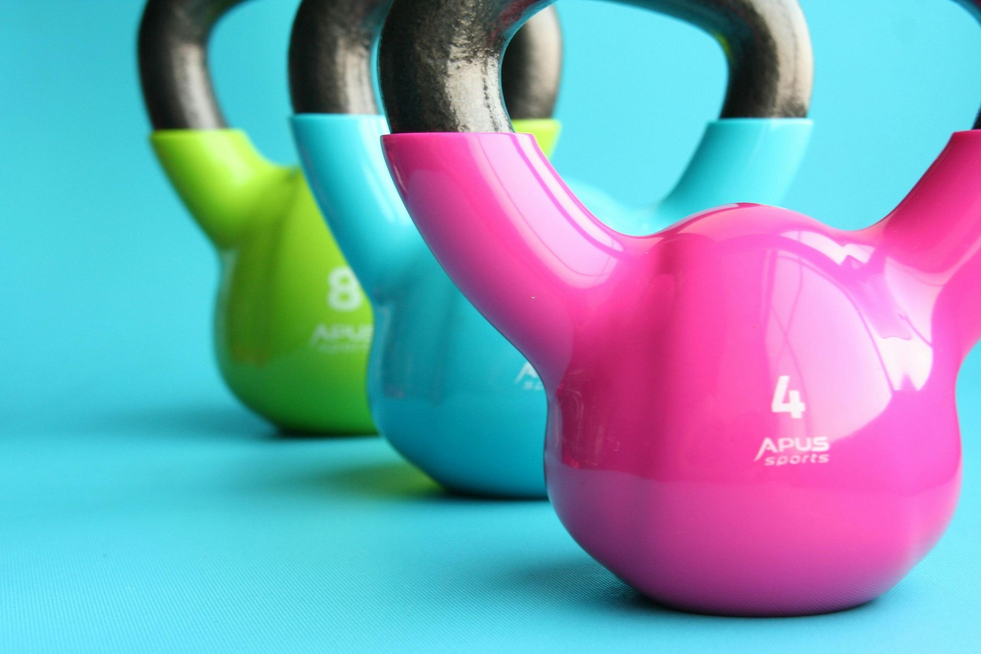 Three different colored kettlebells are lined up on a blue surface.