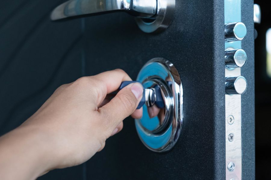 Una mano inserisce una chiave con la parte superiore blu nella serratura metallica di una porta scura e ruvida.