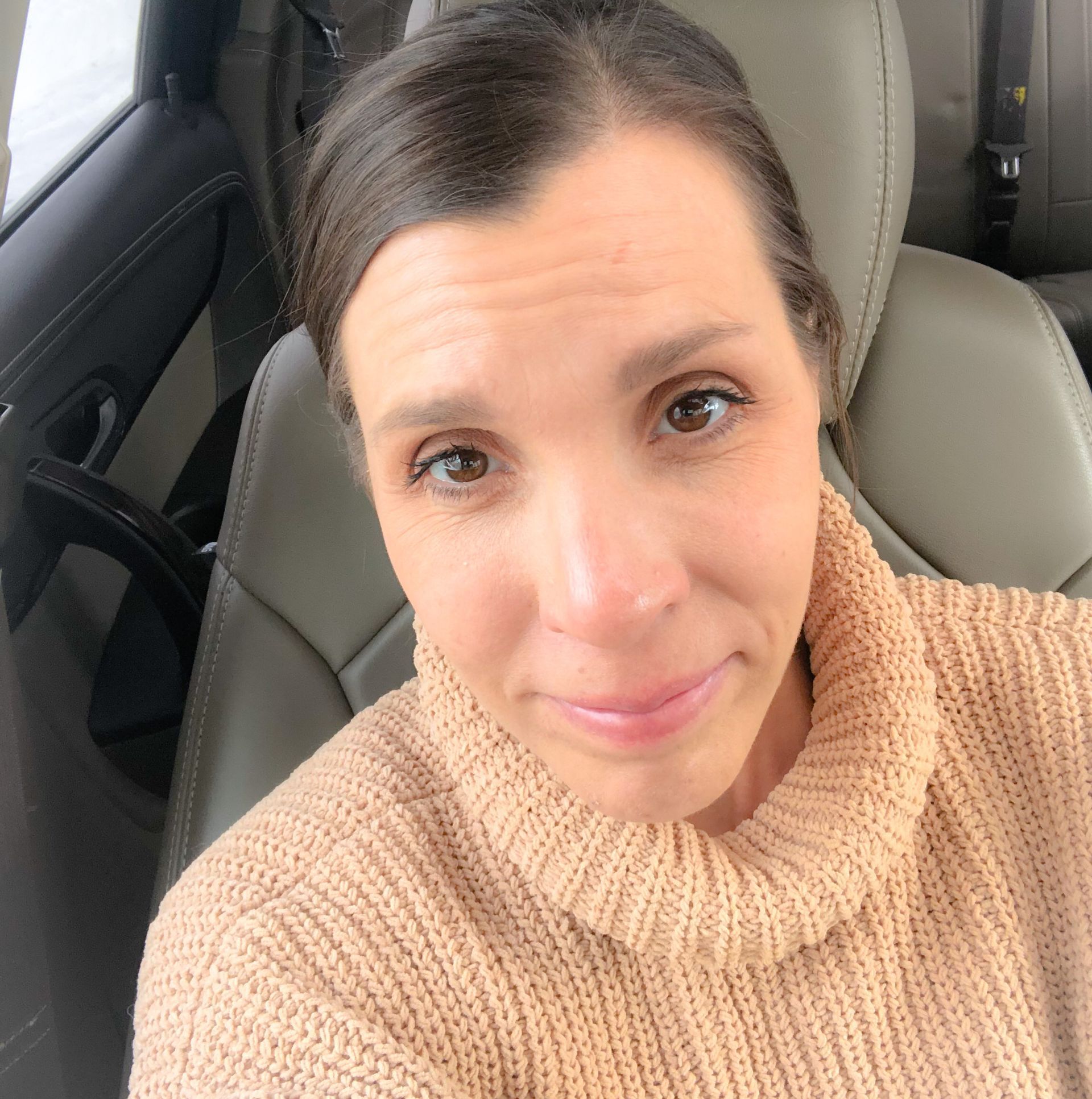 Amy in SUV with hair pulled back, closed lip smile and carmel colored turtleneck sweater
