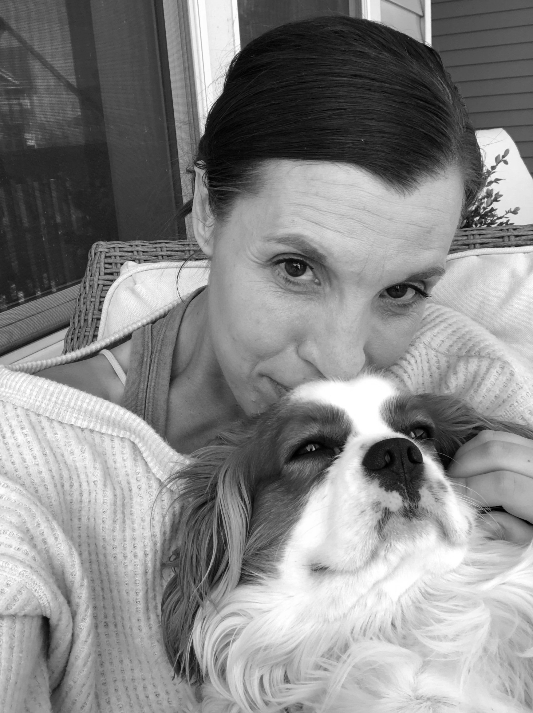 Black and white photo of Amy and Dog on proch sitting. Amy kissing top of Cooper's head with happy look.