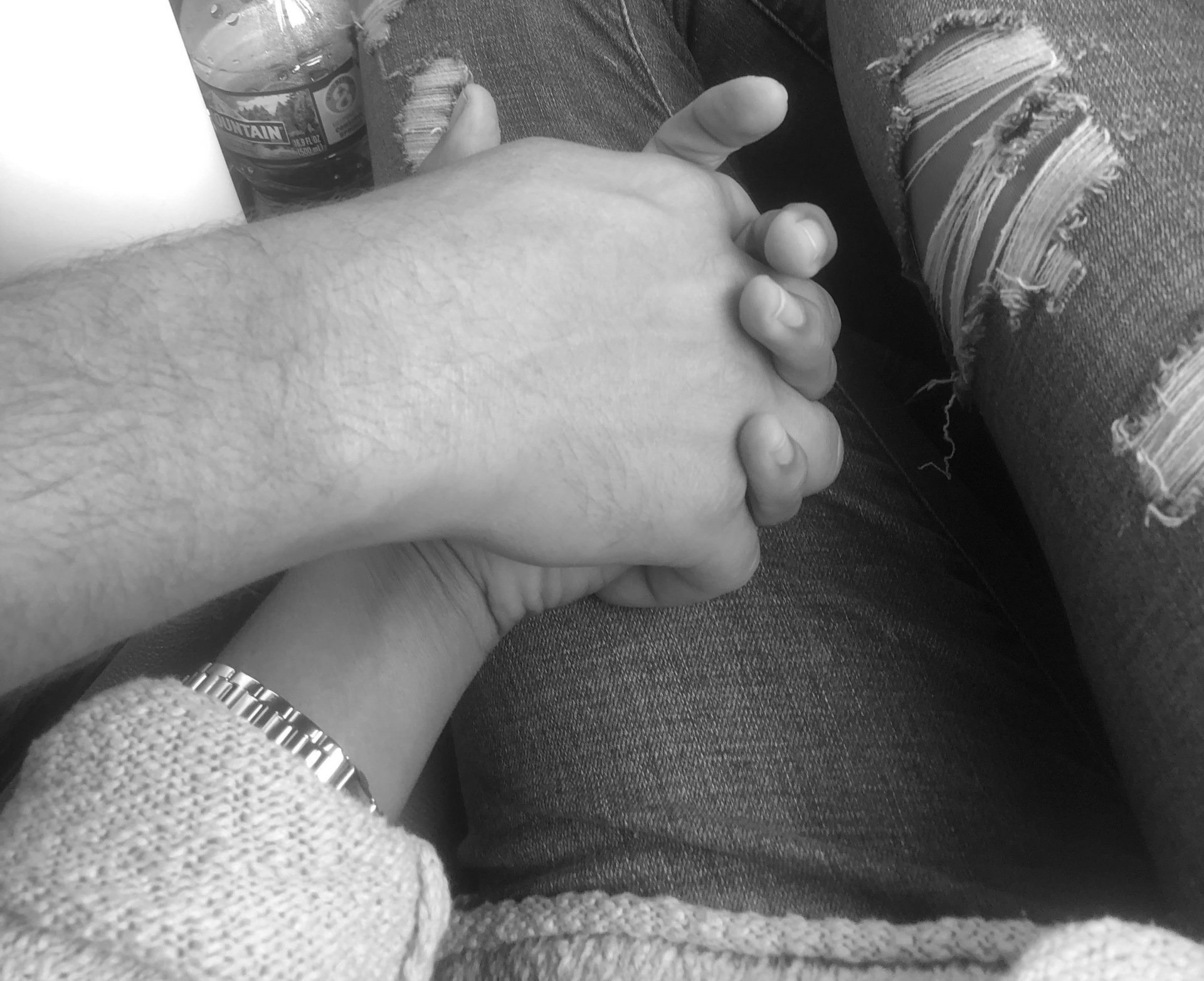 randy and amy holding hands in car black and white photo. Both hands resting on lap with jeans