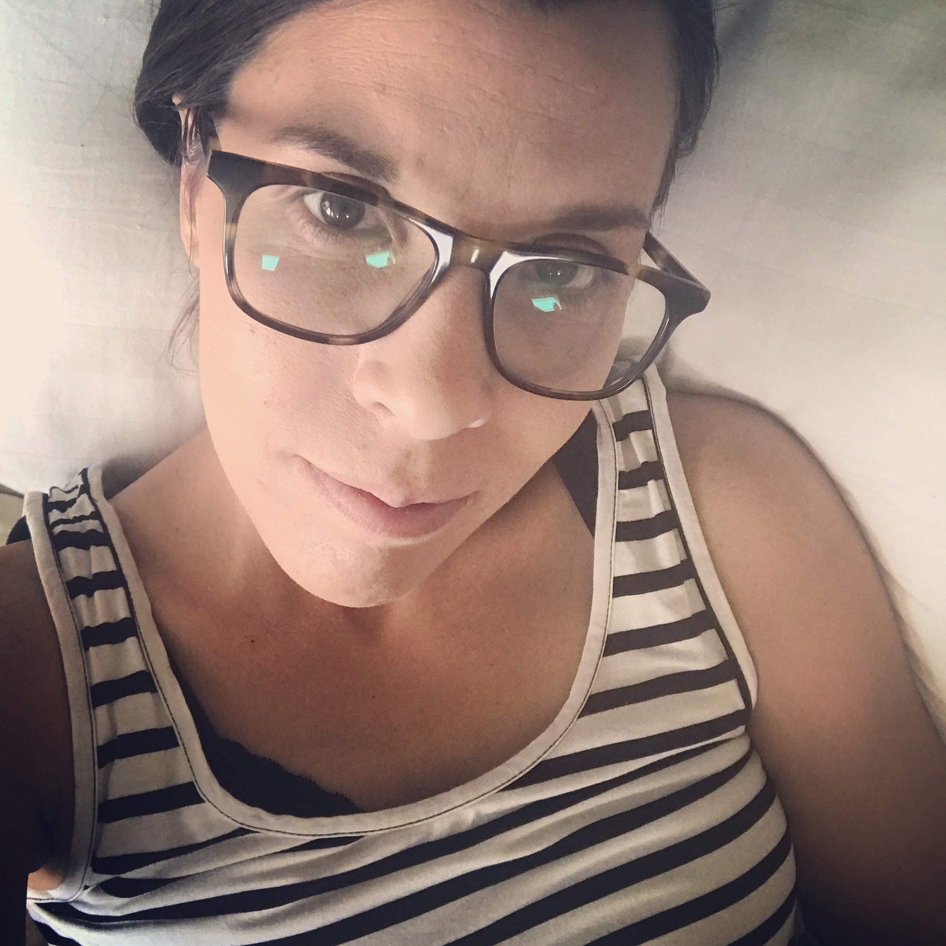 amy with black and white striped tank top and glasses on. Laying in bed with selfie photo.