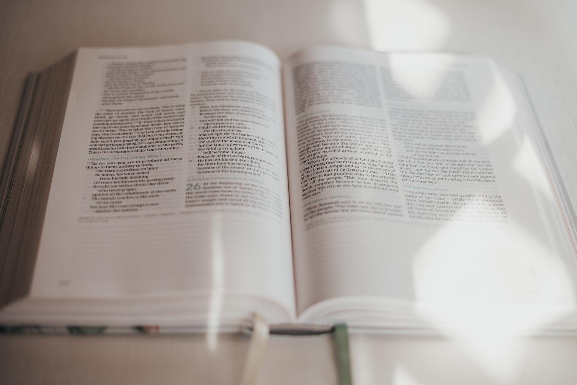 open bible with attached string bookmark hanging on sitting on table and sun shadows over it