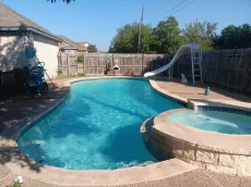 A large swimming pool with a slide and a hot tub in the backyard of a house.