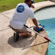 A man is kneeling on the edge of a swimming pool.