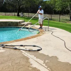 A man is cleaning a swimming pool with a hose