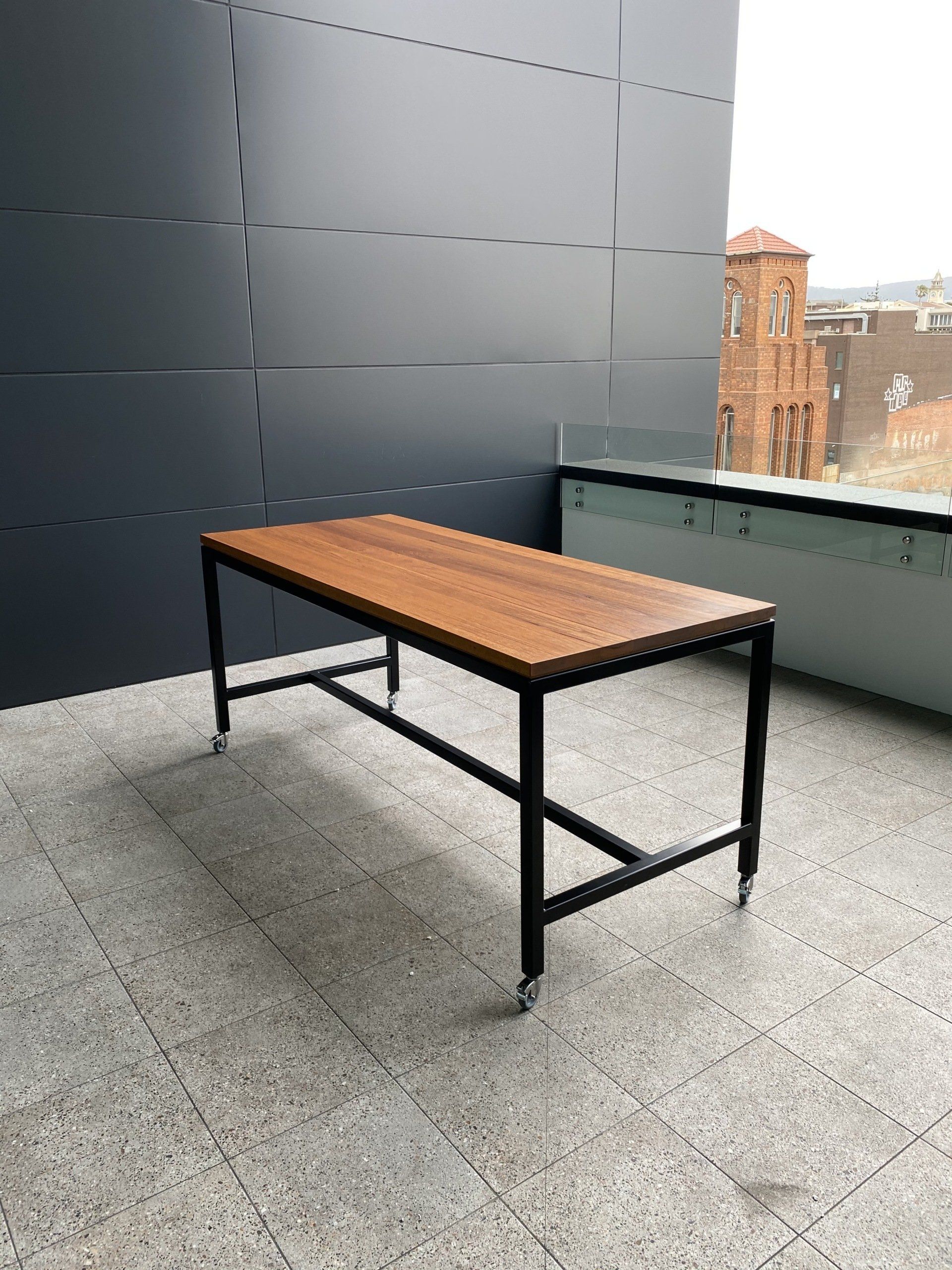 A Wooden Table With Wheels Is Sitting On A Patio In Front Of A Building — Marlix Custom Timber Furniture Design and Joinery in Southern Highlands, NSW