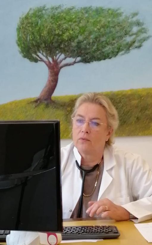 Medico in camice bianco, stetoscopio, che guarda lo schermo del computer, con un dipinto di un albero sullo sfondo.