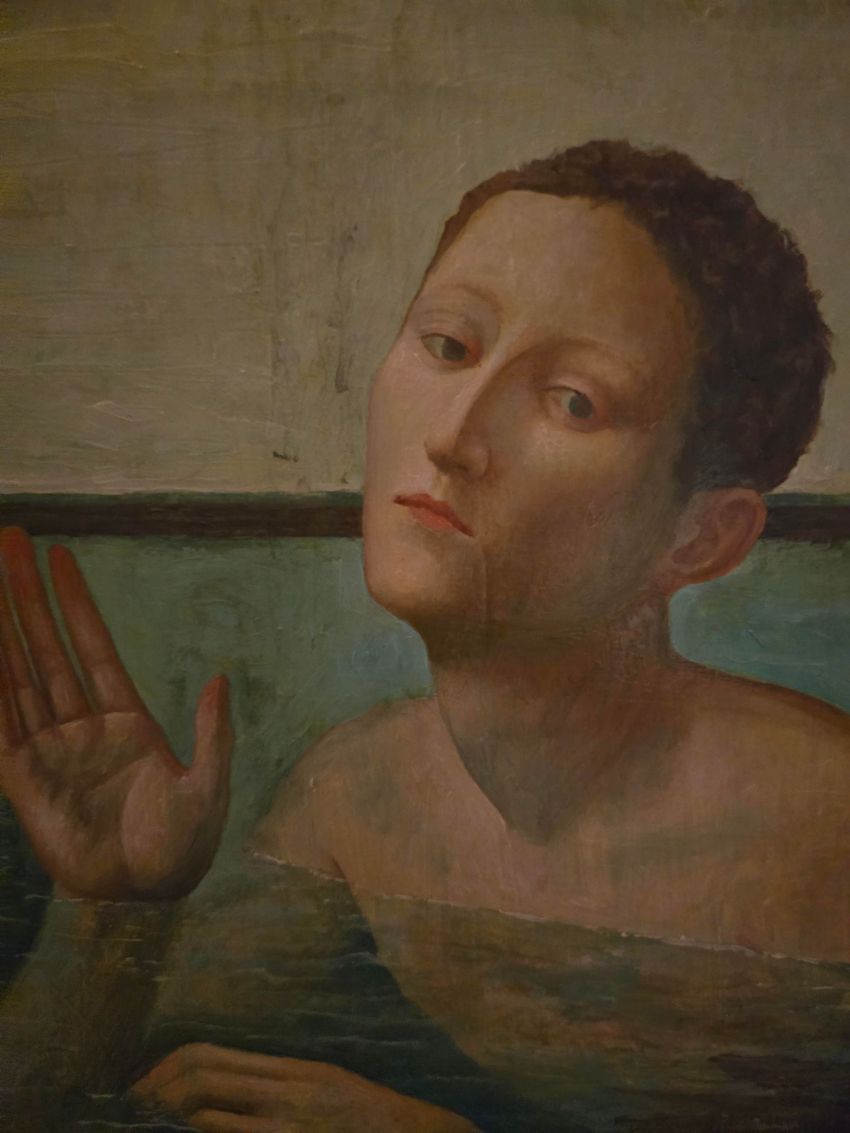 Persona in una vasca da bagno che alza una mano. Acqua e pareti sono visibili, con toni freddi.