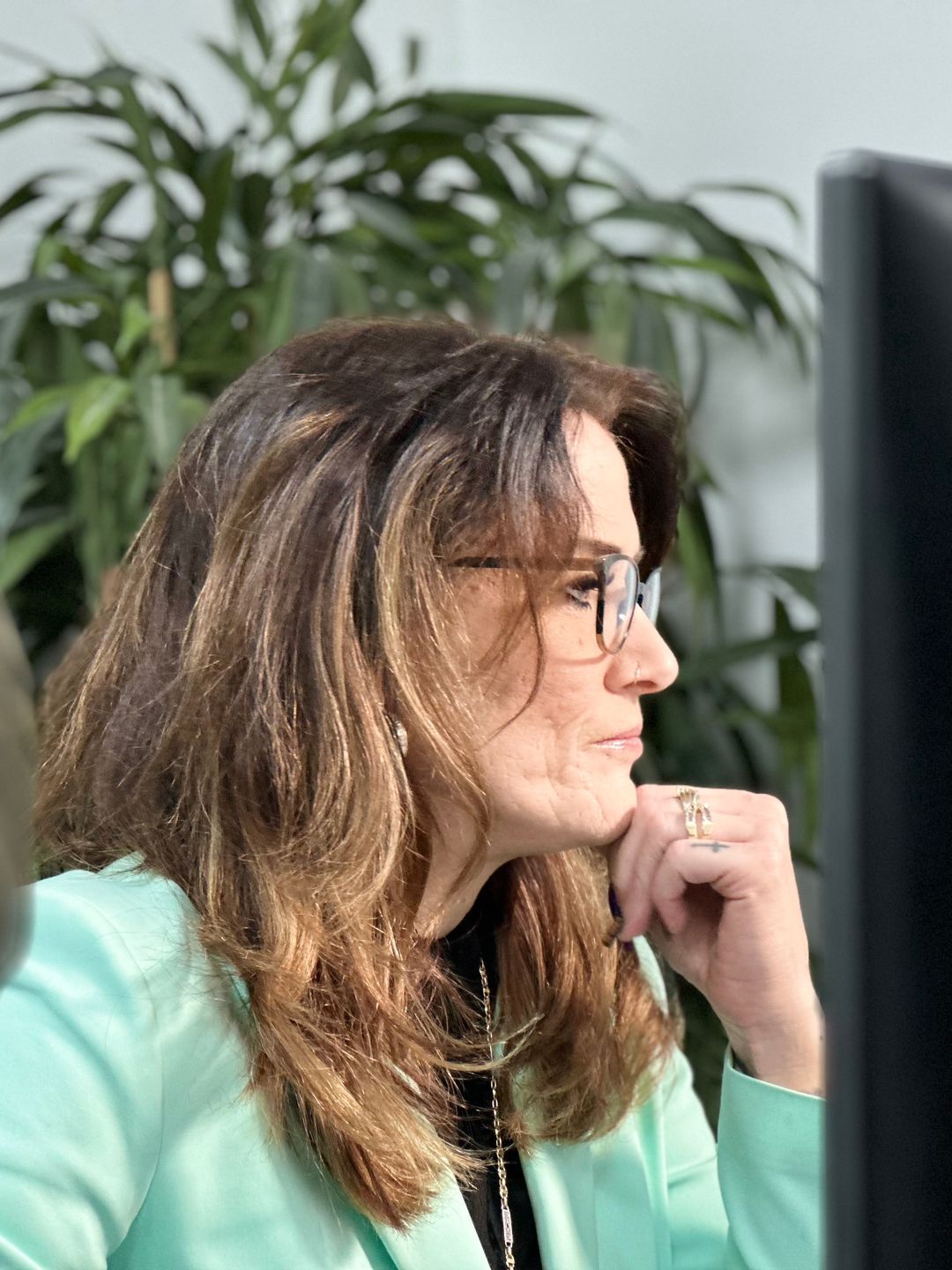Woman with brown hair and glasses in a light green blazer looks at a computer screen.