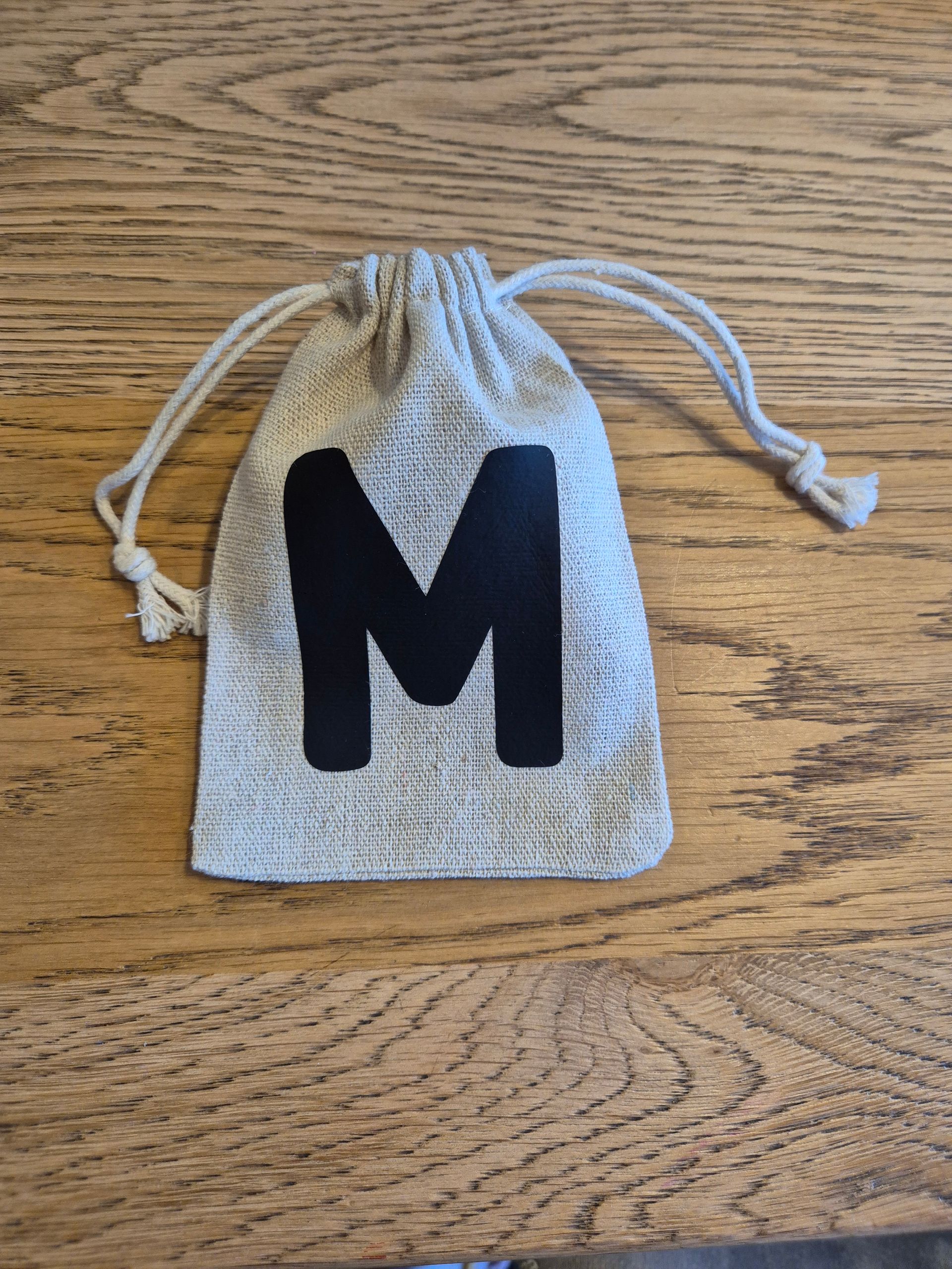 Klein beige tasje met trekkoord en een glinsterende letter