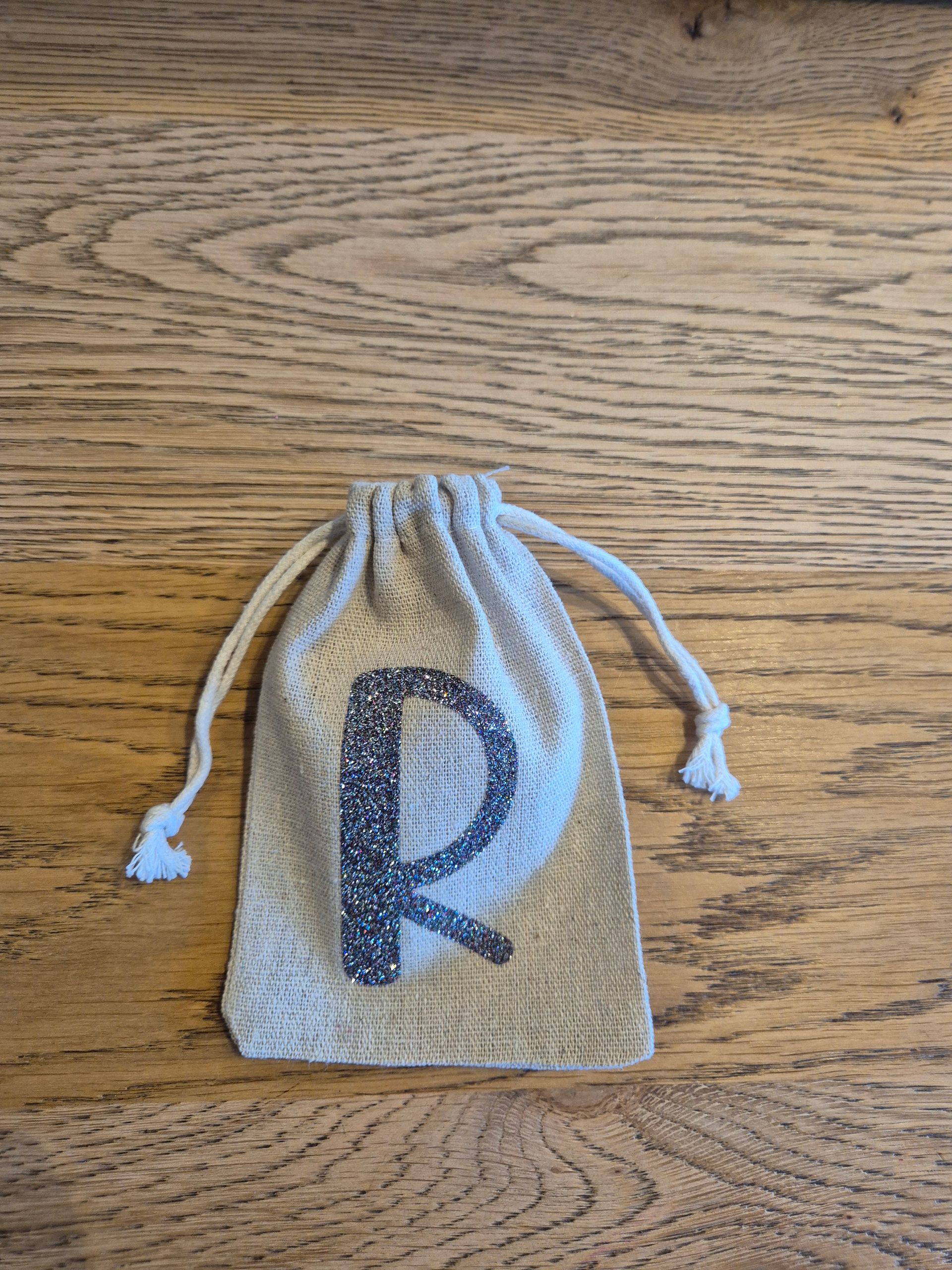 Klein beige tasje met trekkoord en een glinsterende letter