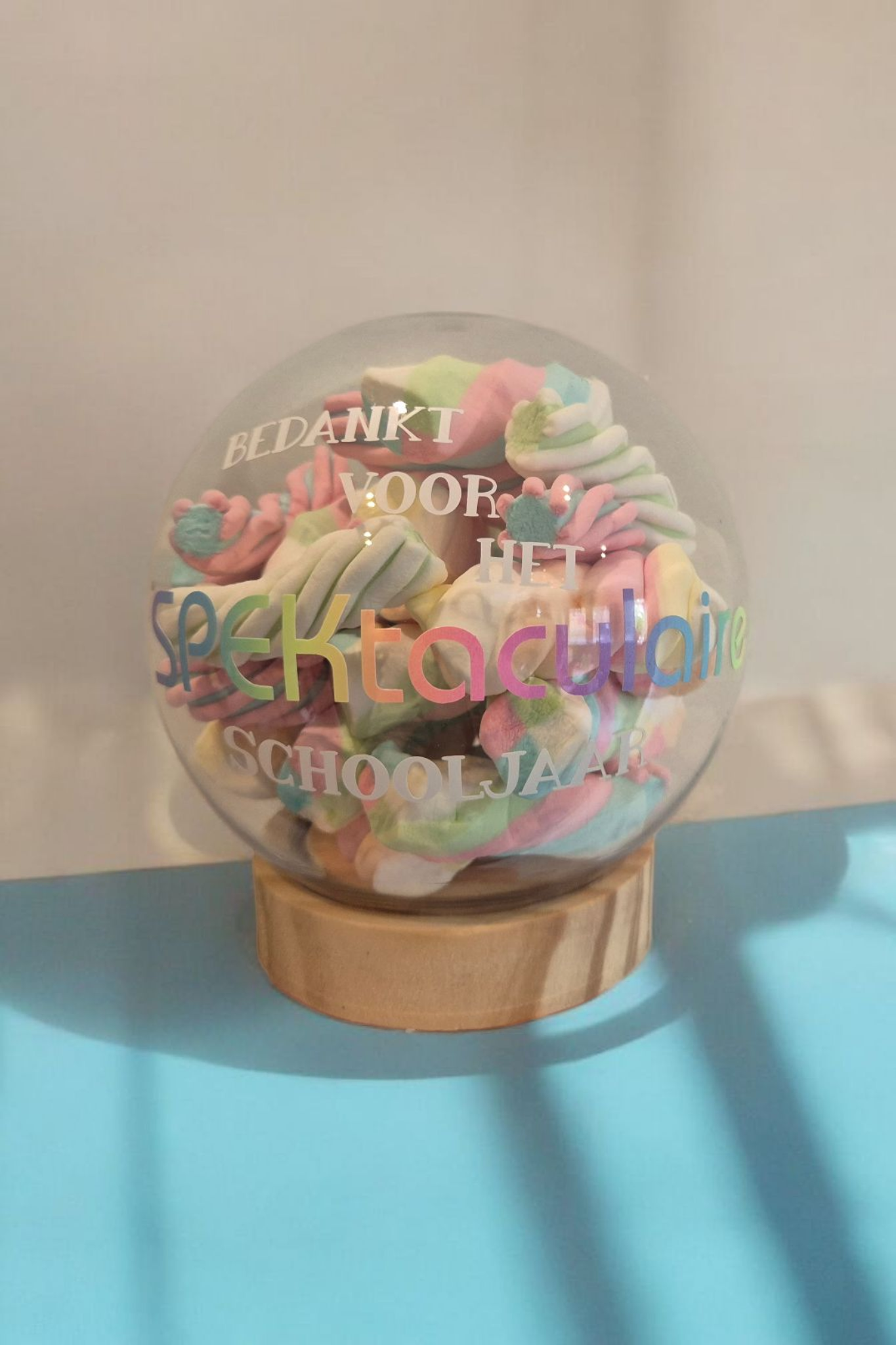 Een transparante bol gevuld met marshmallows op een houten voet met de tekst: 