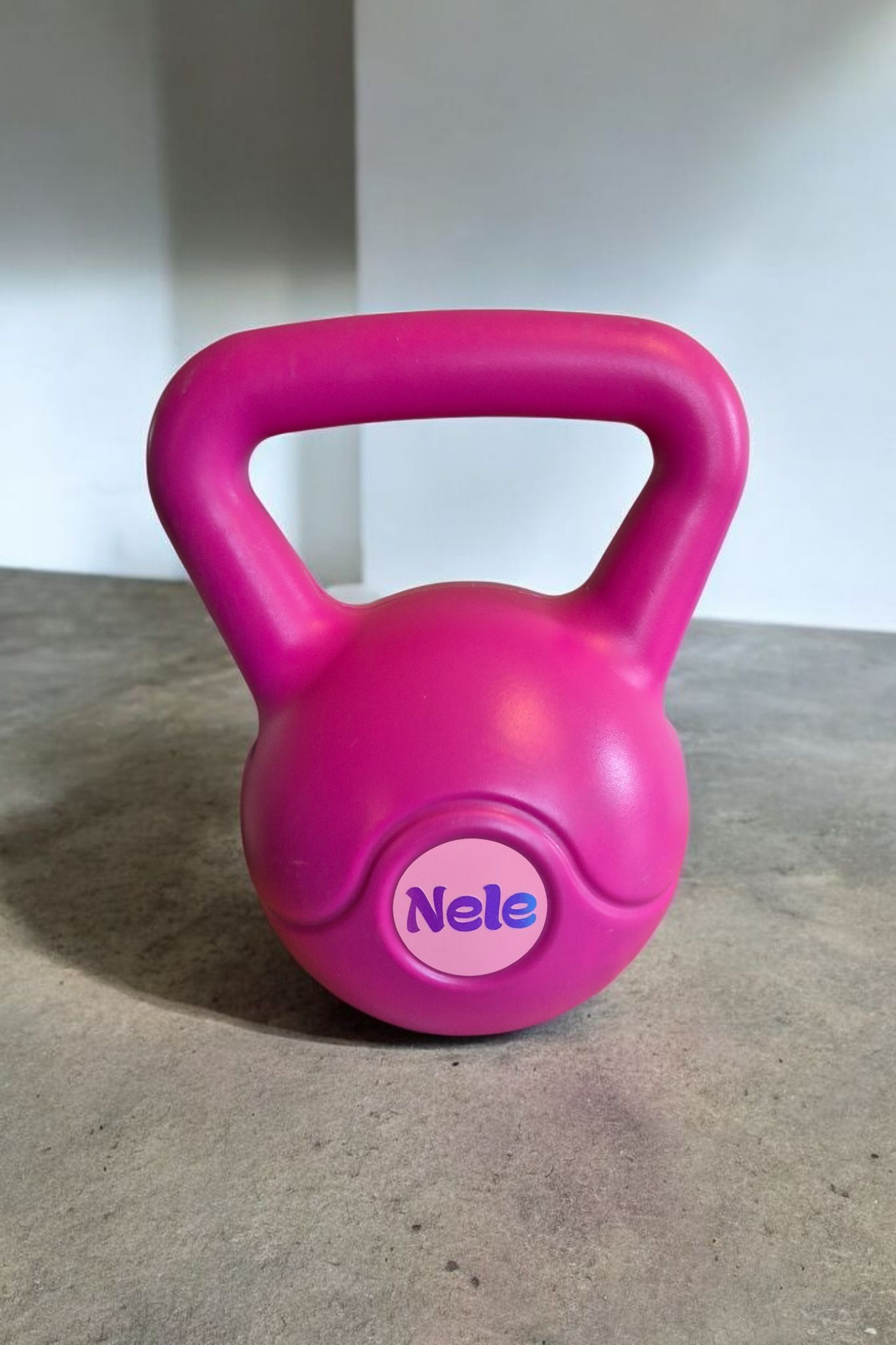 Roze kettlebell op een betonnen ondergrond met een witte muur op de achtergrond, met de naam 