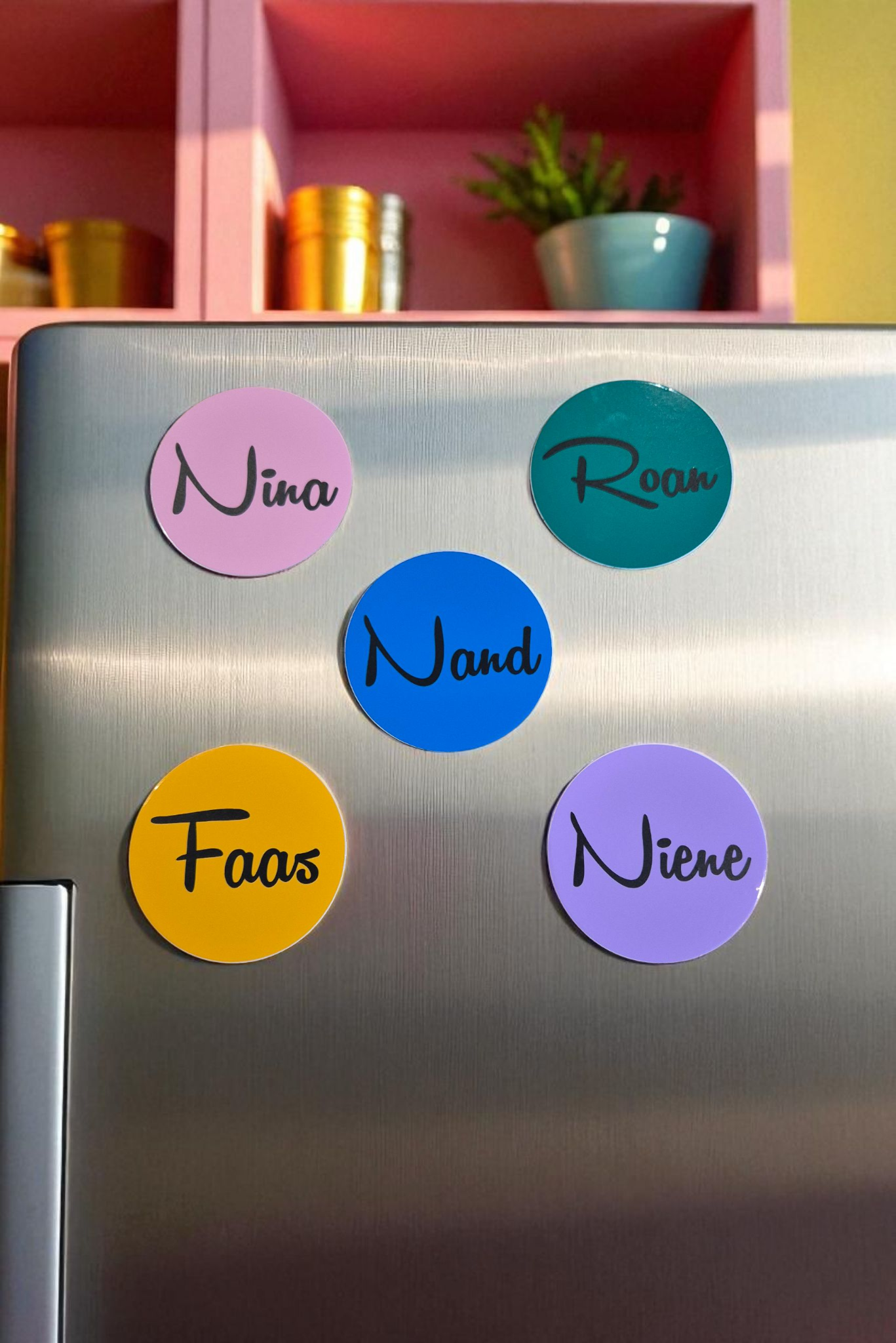 Vijf kleurrijke, ronde magneten op een verweerde houten ondergrond, elk met een naam in zwarte letters.