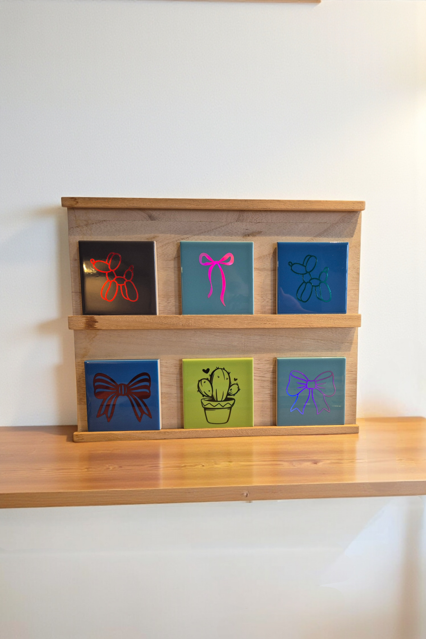 Houten plank met zes kleurrijke tegels met gegraveerde motieven (strikjes, cactus).