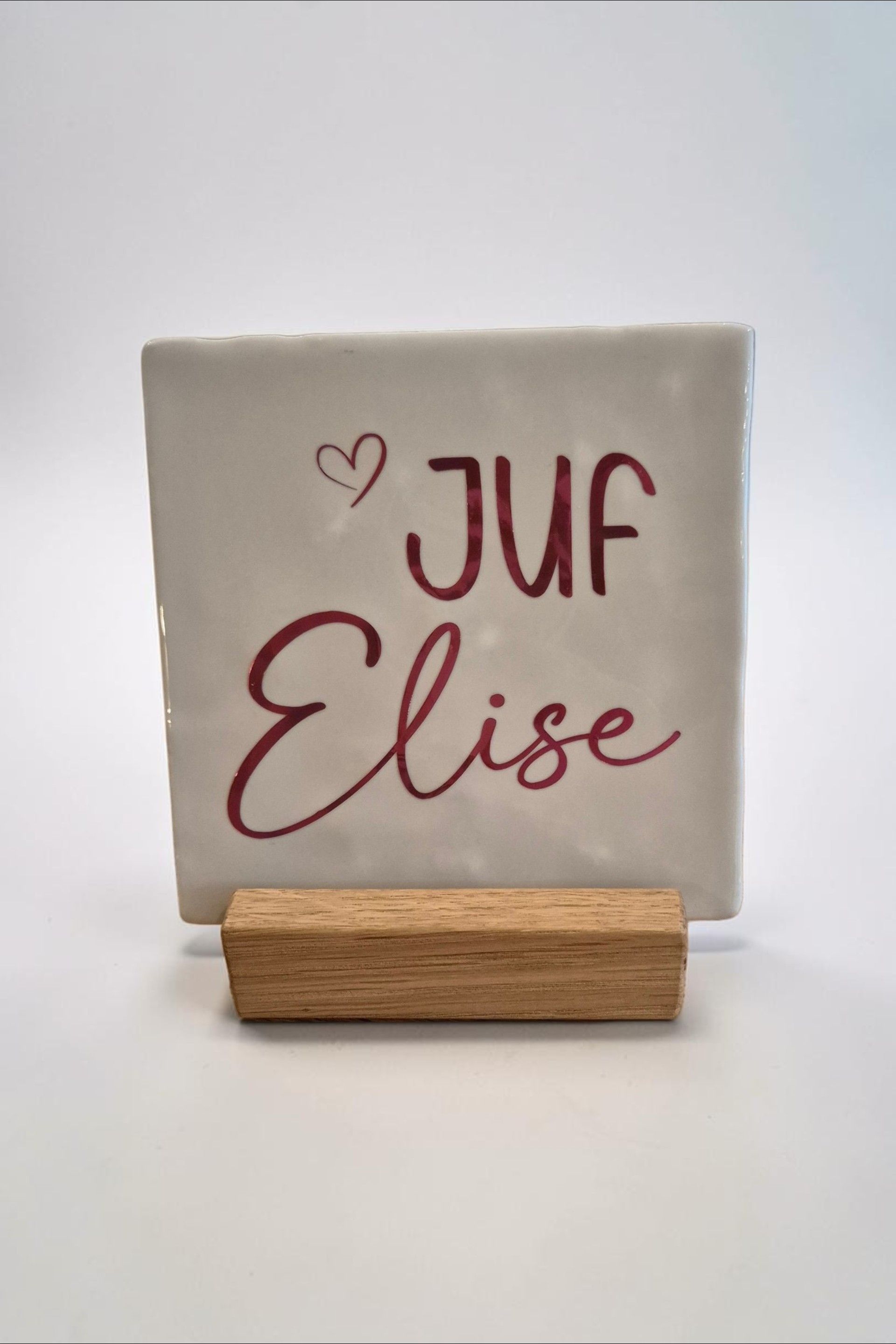 Drie tegeltjes met sierlijke letters, voor meester of juf, op een rustieke houten tafel tegen een witte muur.
