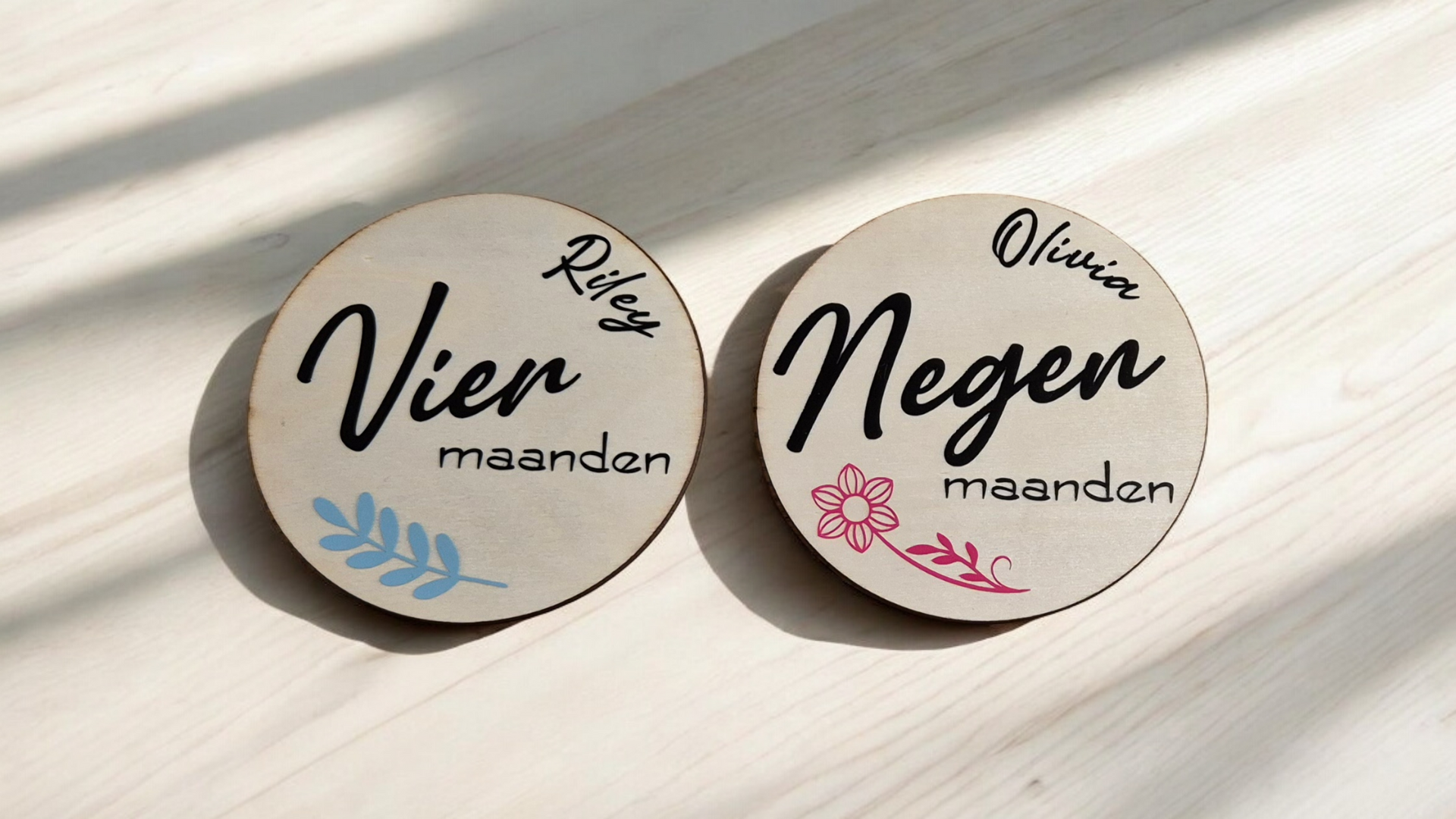 Twee houten cirkels met daarop namen en de maanden. Op de ene staat een blauw blad, op de andere een roze bloem.