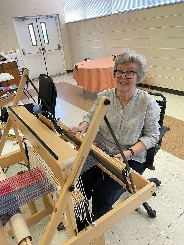 A fort worth weaver's guild member  sitting at a loom at a meeting