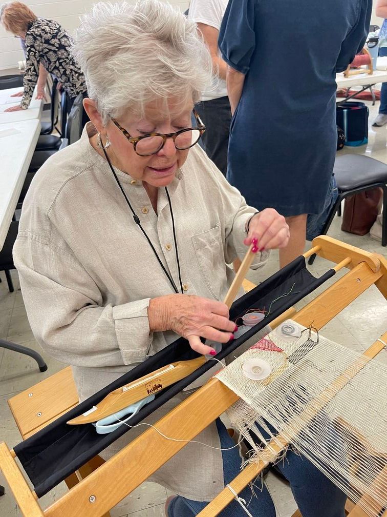 A fort worth weaver sitting at a table working on a loom.