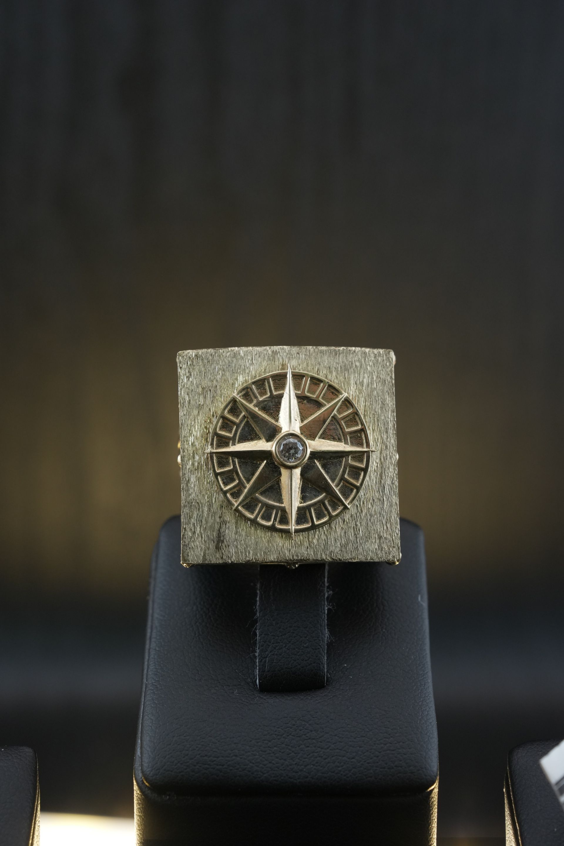 Gold compass ring on black display stand against a dark background.