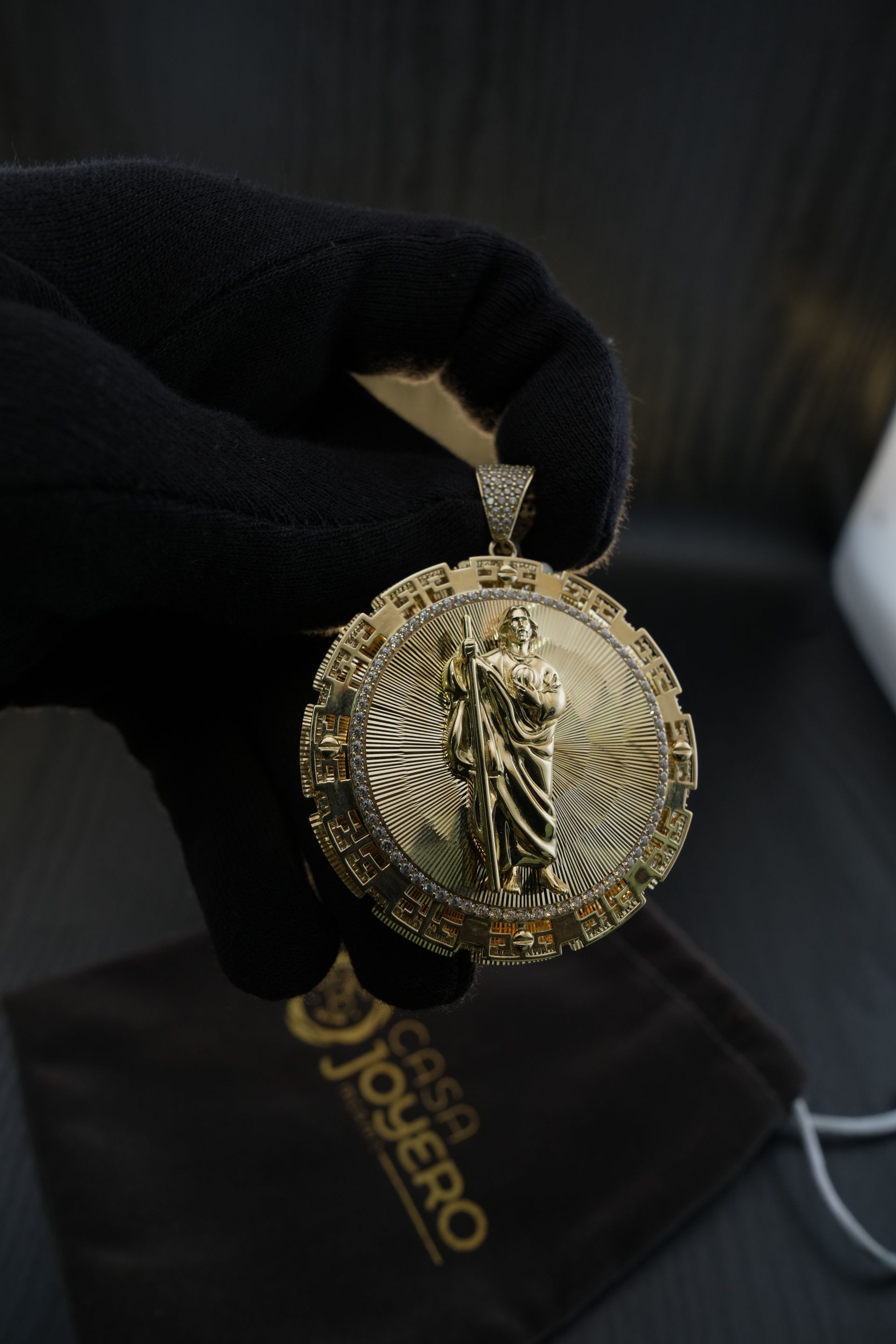 Gold pendant of Saint Jude held by a gloved hand, with