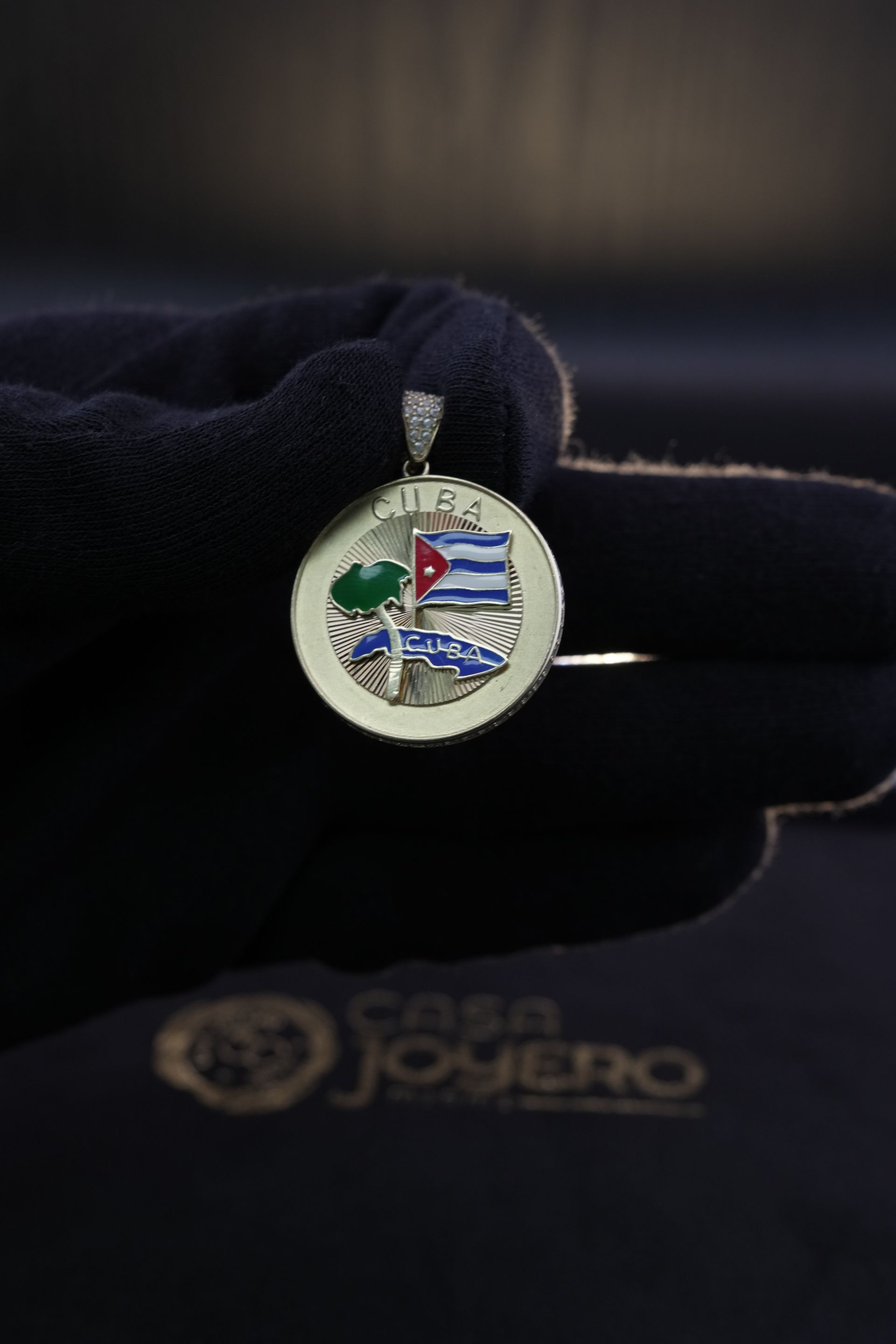 Gold pendant with Cuban flag design, held by a gloved hand.