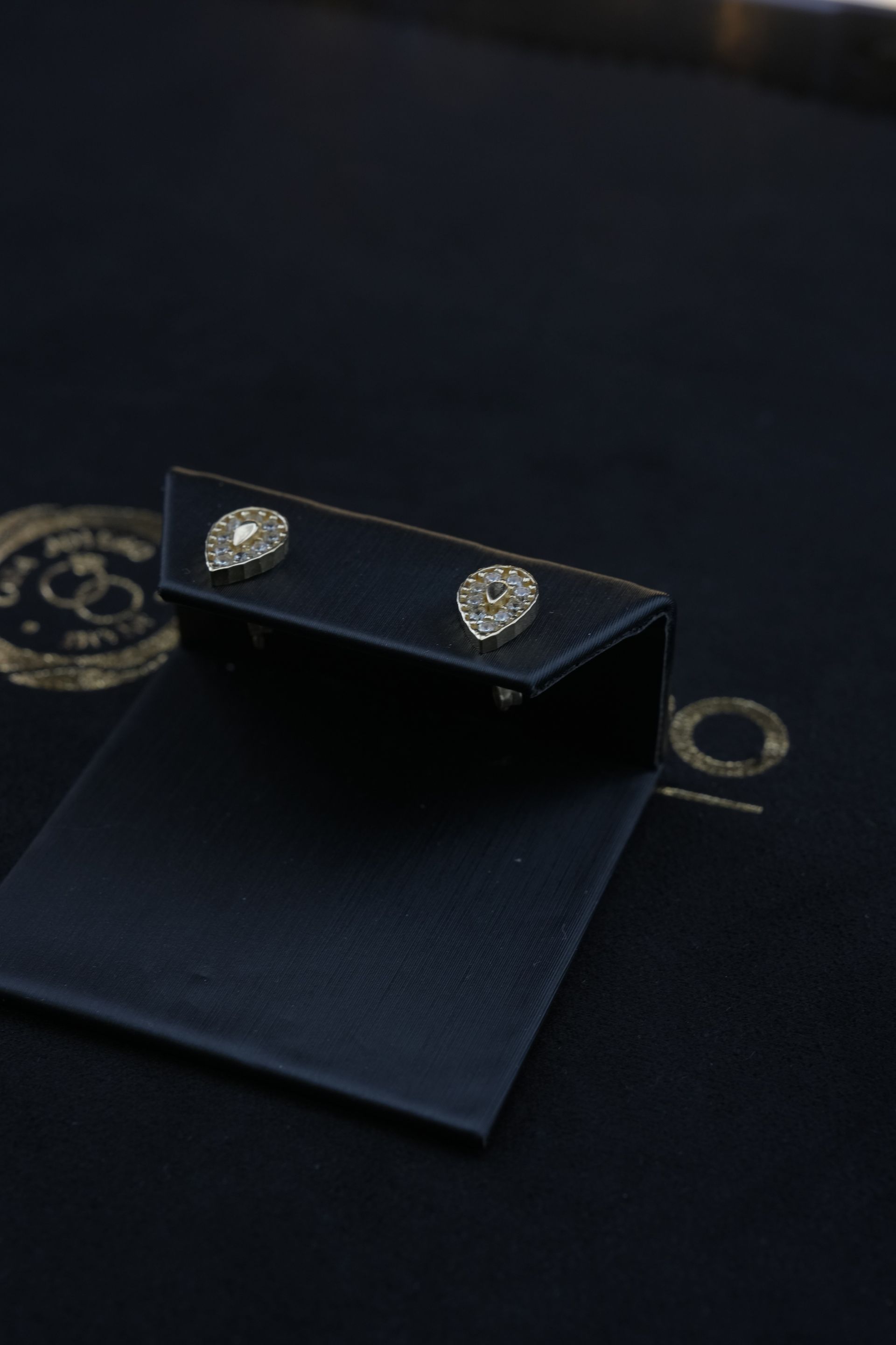 Diamond stud earrings on a black display stand over a black surface, likely packaging.