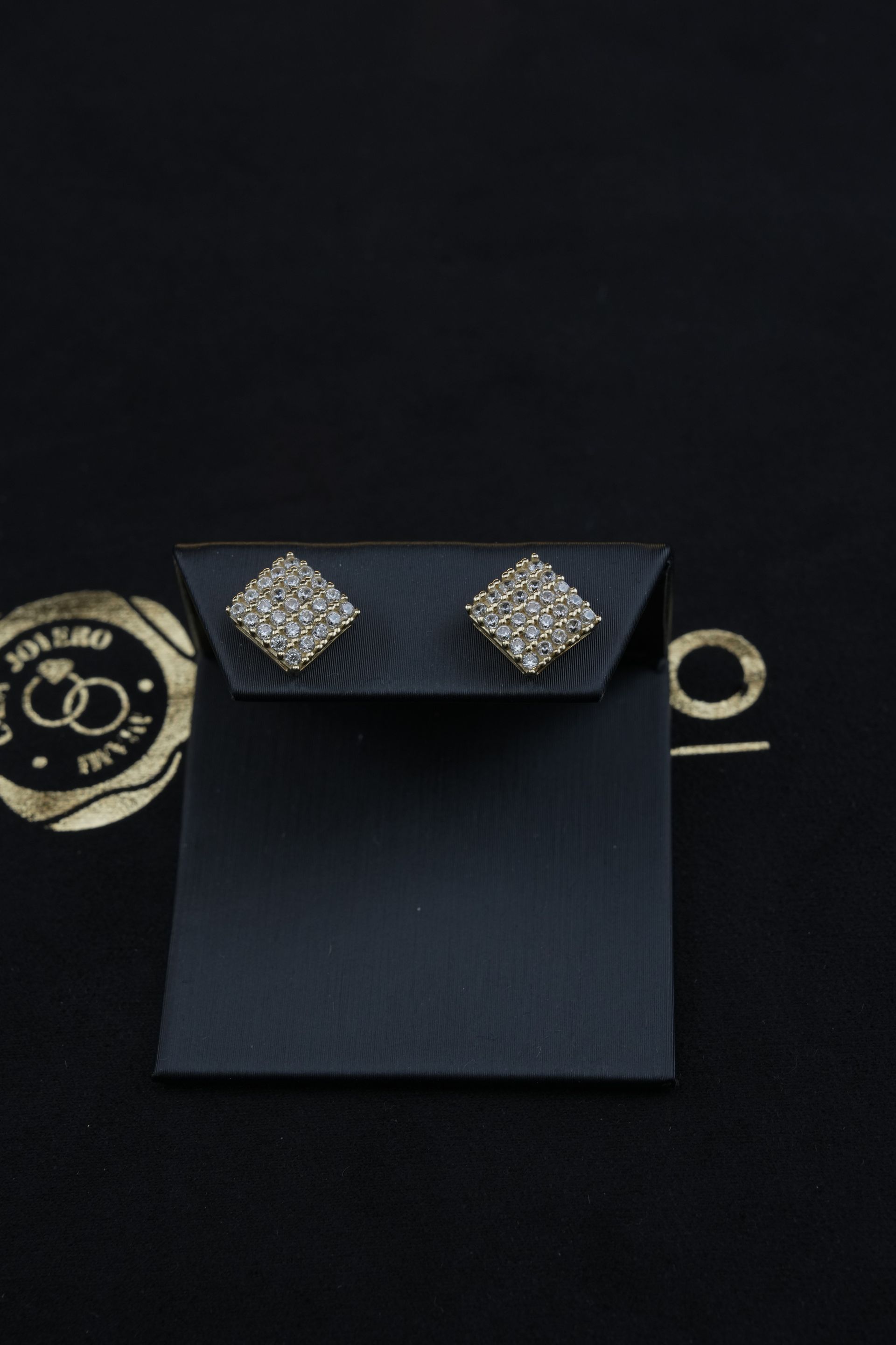 Square diamond stud earrings on a black display card against a black background.