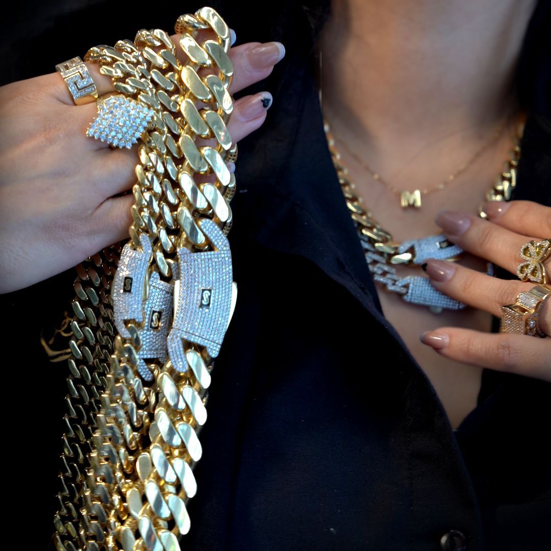 Person displaying several gold jewelry pieces, including necklaces, rings, and a large chain with jeweled panther-head clasp.