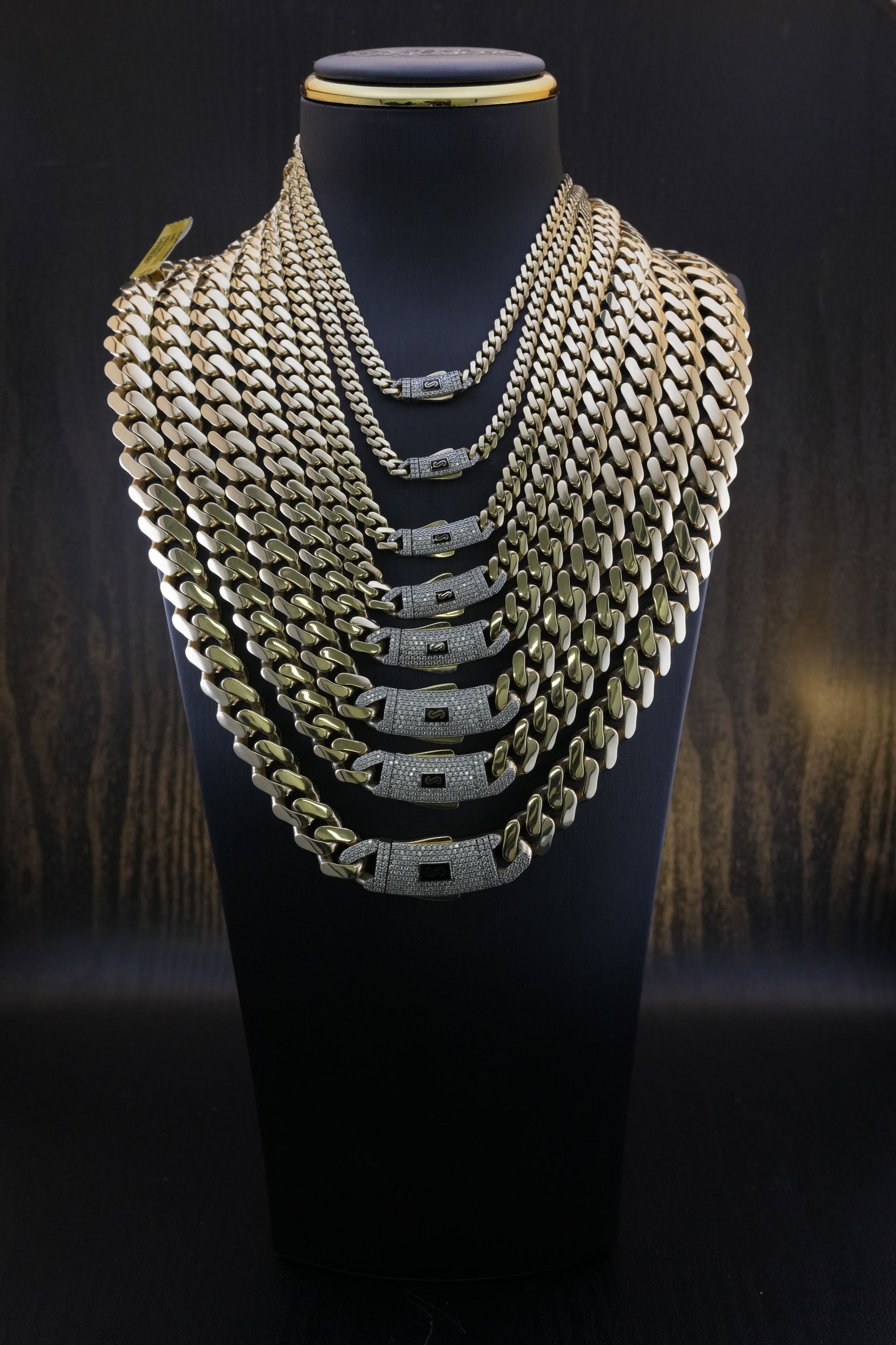 Gold chain necklaces displayed on a black mannequin against a dark background.