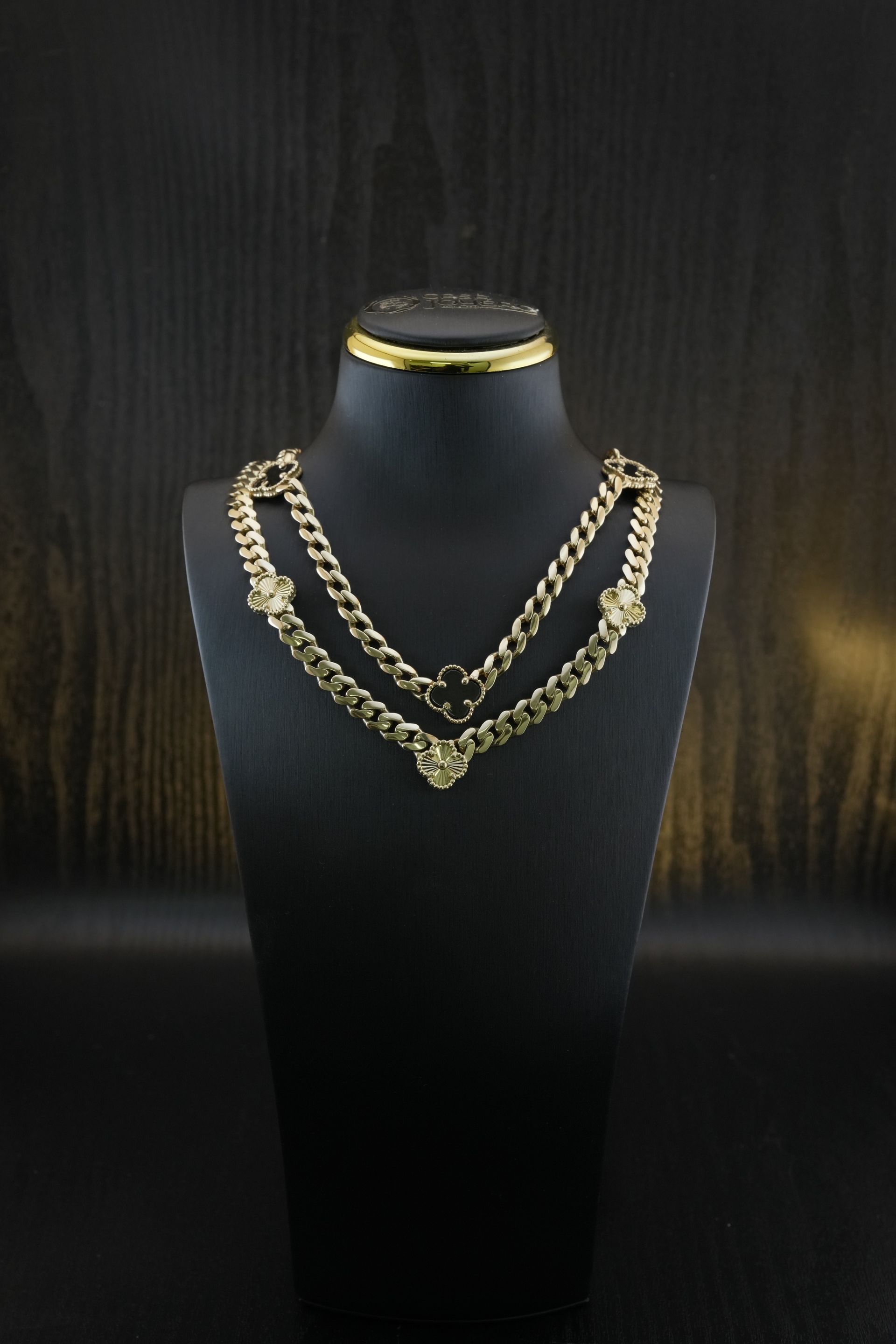Gold chain necklaces displayed on a black mannequin against a dark wooden background.