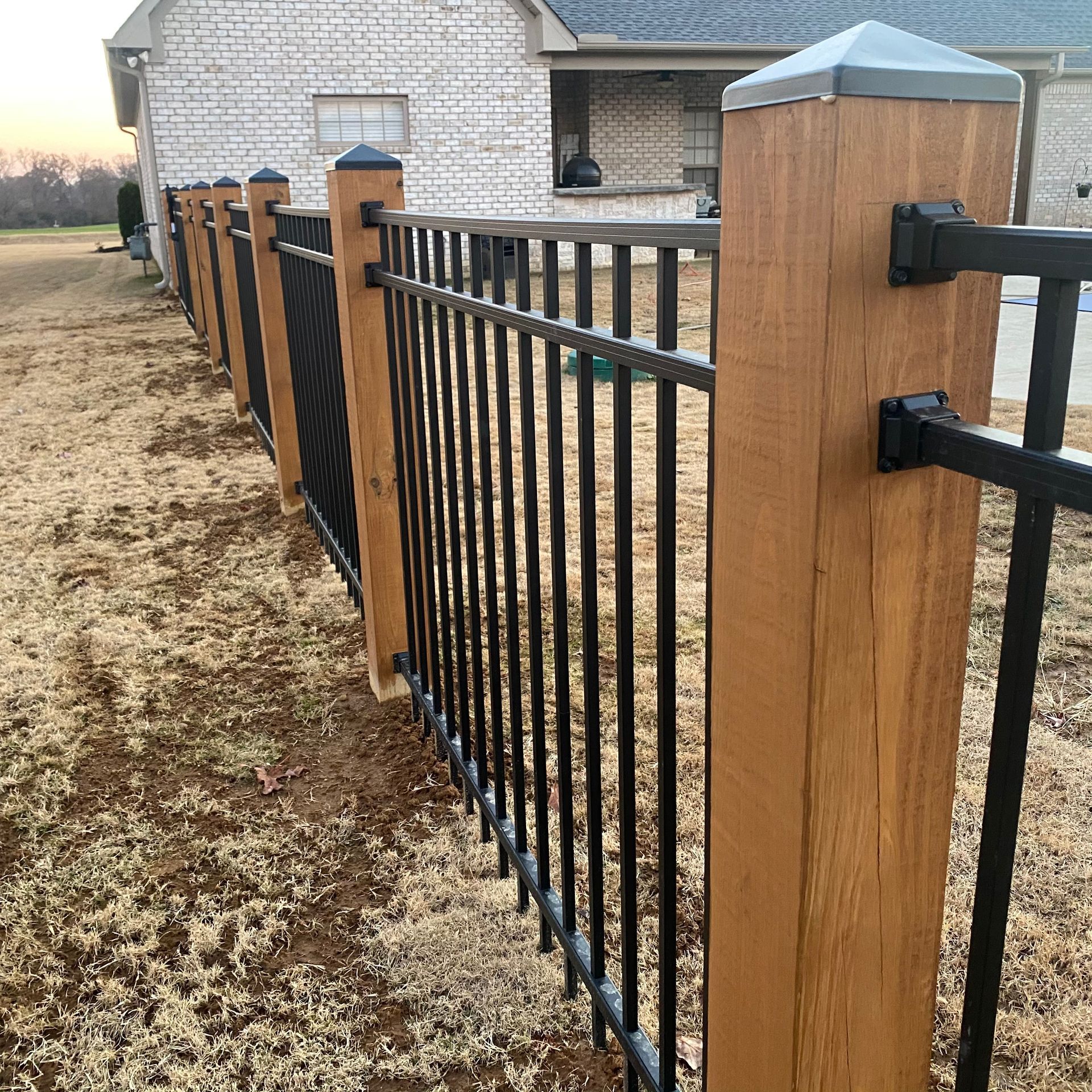 A residential fence featuring black metal panels mounted between natural wood posts with dark gray post caps.