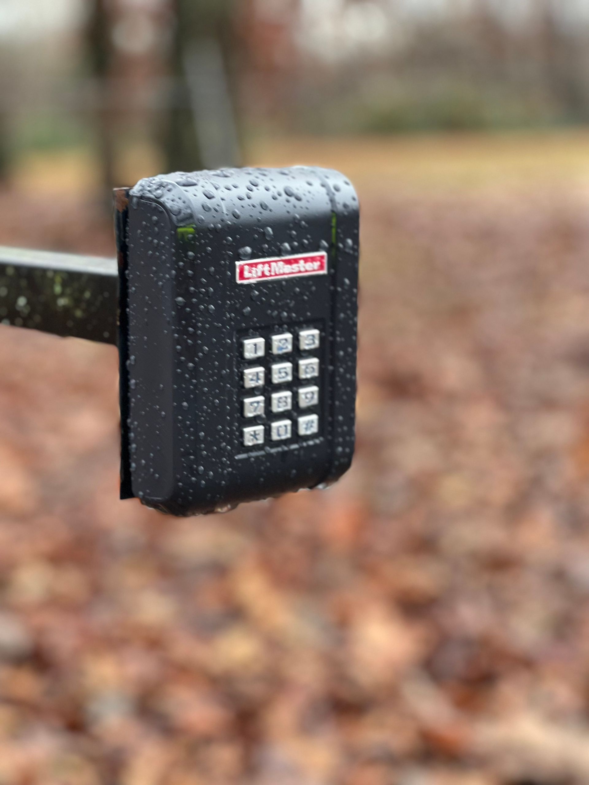 A black LiftMaster wireless keypad mounted on a post outdoors in the rain.