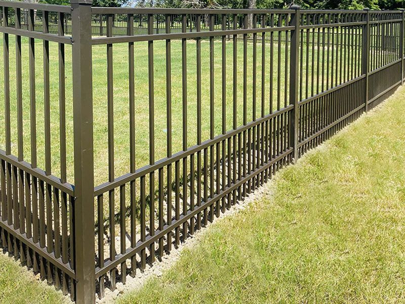 A dark bronze-colored metal puppy-picket fence surrounding a grassy lawn.