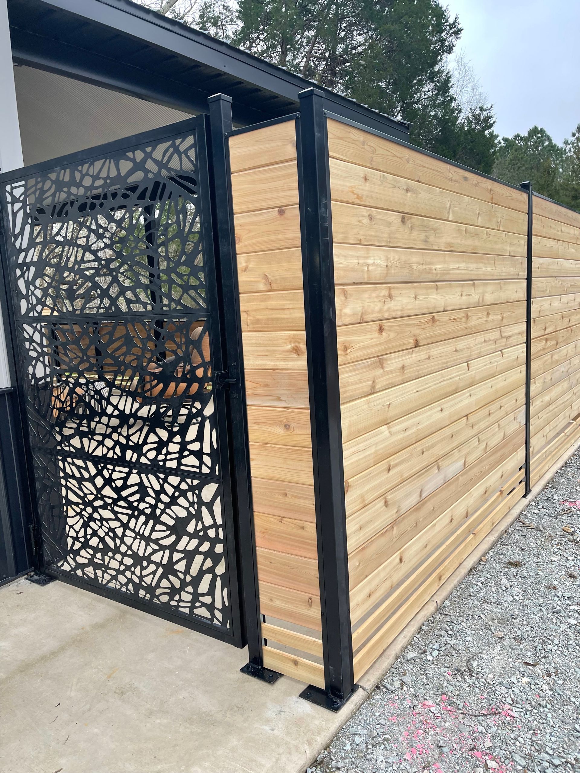 A modern fence with horizontal wood slats and a black metal gate featuring a decorative, abstract, organic pattern.