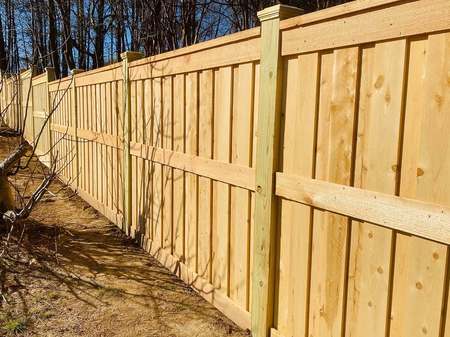 A long wooden privacy fence with vertical panels and horizontal bracing, extending into the distance outdoors.